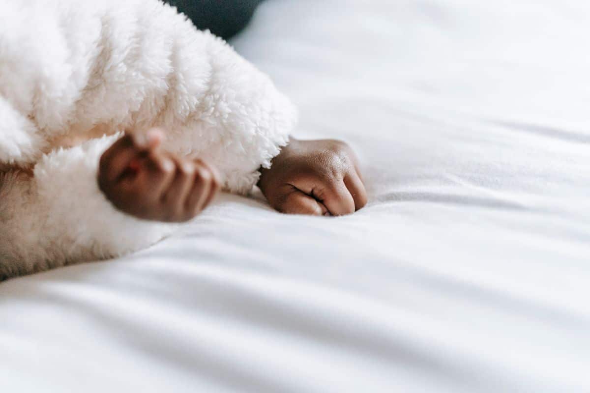 Baby in white sweater laying on white bedsheets